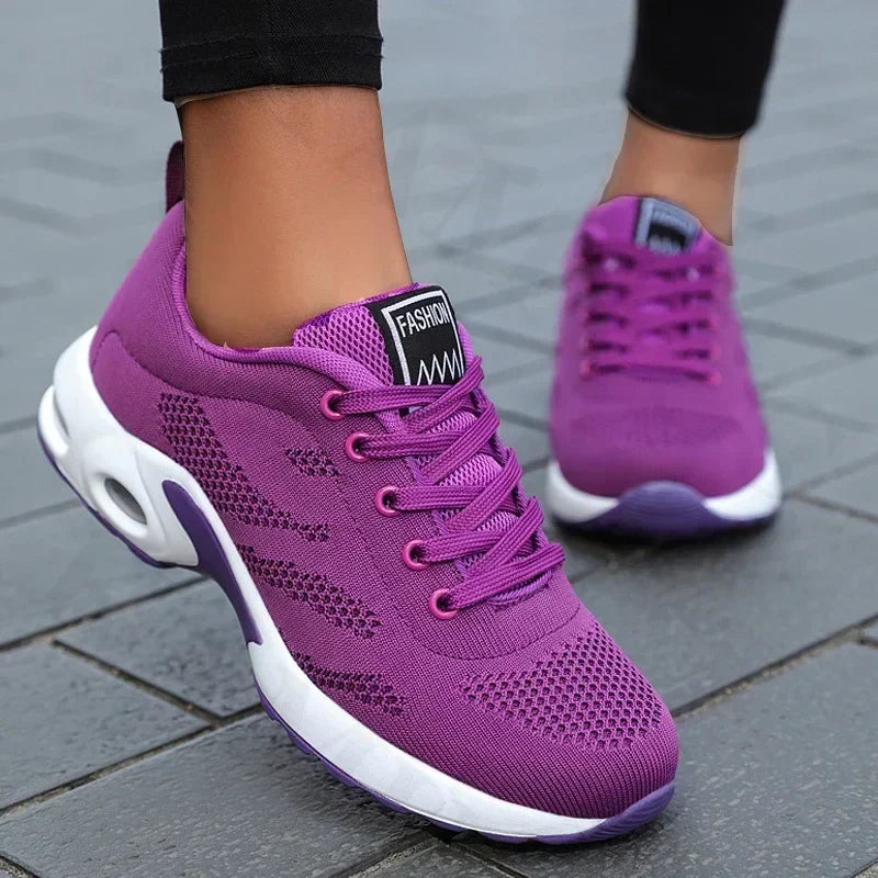 Chaussures de sport violettes pour femme sur pavé gris, design moderne avec semelle blanche, idéales pour la course et le fitness.