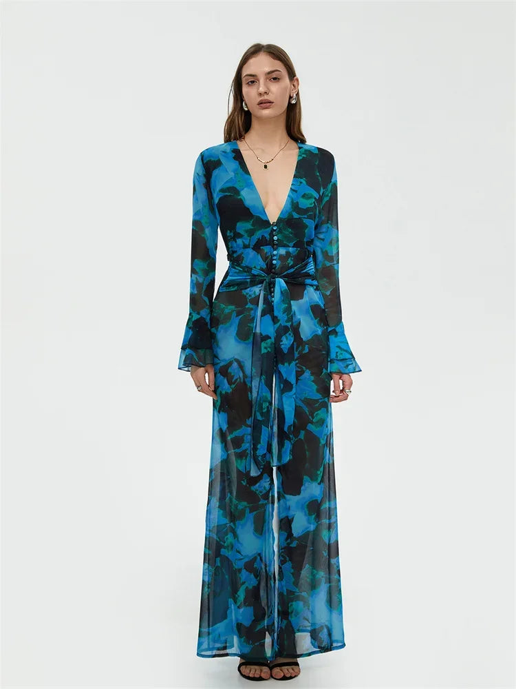 Robe longue bleue à motifs floraux, manches longues, décolleté plongeant, ceinture nouée, portée par une femme. Mode élégante et tendance.