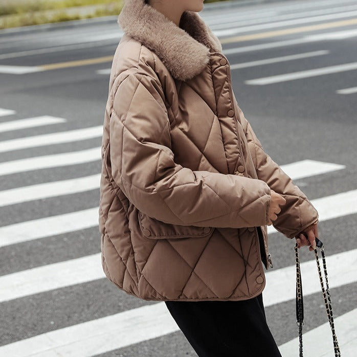Veste matelassée marron avec col en fourrure, portée par une personne traversant un passage piéton. Mode hiver, style urbain, tendance.