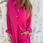 Femme portant une chemise rose vif en lin, manches retroussées, devant un mur texturé. Mode estivale, tenue décontractée, style tendance.