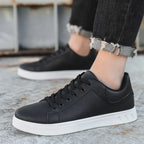 Chaussures noires en cuir pour homme, style baskets, semelle blanche, portées avec un jean noir retroussé. Mode urbaine, tendance décontractée.