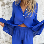 Femme portant un ensemble bleu vif, chemise ample et pantalon taille haute, devant un mur texturé. Mode estivale, tenue décontractée élégante.