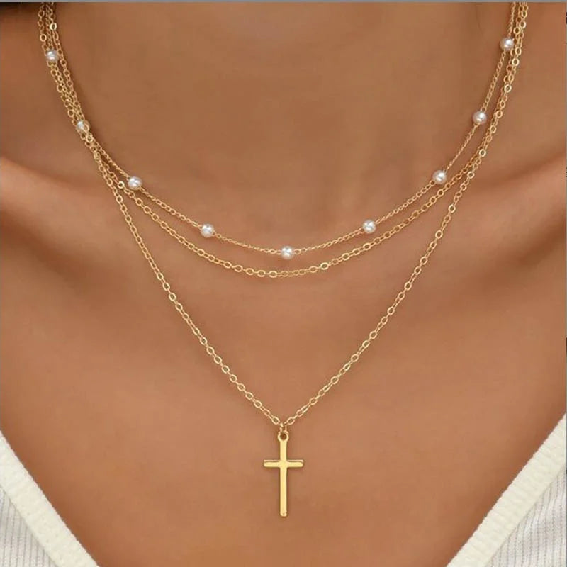 Collier en or à trois rangs avec pendentif croix et perles, porté sur un décolleté. Bijoux élégants, tendance mode, accessoires féminins.