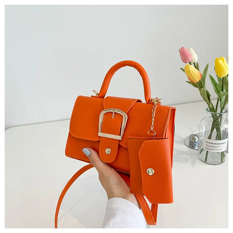 Sac à main orange vif avec boucle dorée, porté à la main. Accessoire de mode tendance, idéal pour un look élégant. Tulipes en arrière-plan.