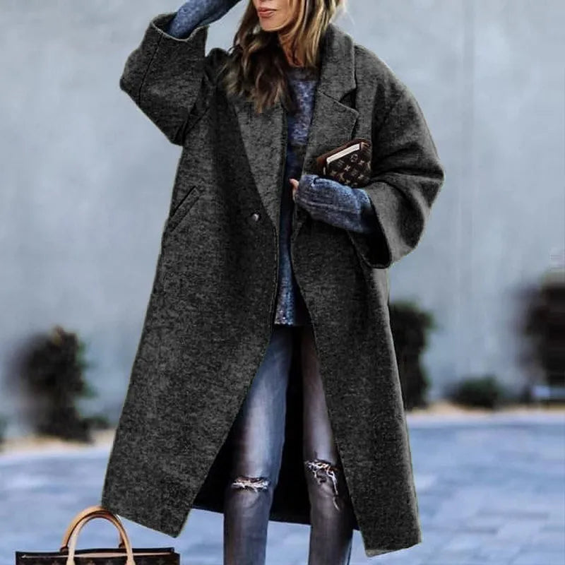Femme portant un manteau gris oversize, jeans déchirés, et gants bleus, tenant un sac à main marron. Mode hiver élégante et décontractée.