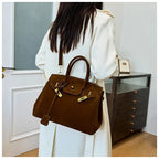 Femme en manteau blanc portant un sac à main marron élégant, style Birkin, dans un intérieur moderne. Mode féminine, accessoires de luxe.