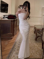 Femme en robe de soirée blanche élégante, posant devant un miroir dans un salon luxueux. Mode glamour, tenue de soirée, style chic.