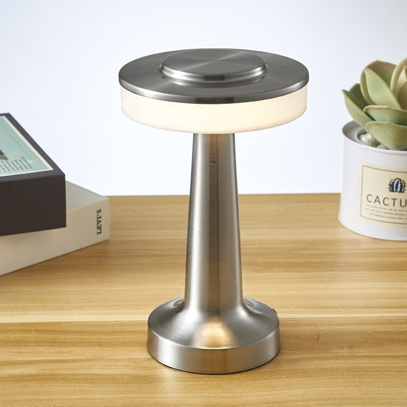 Lampe de table moderne en métal brossé sur bureau en bois, éclairage LED, design minimaliste, à côté de livres et plante succulente.