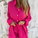 Femme portant une chemise et un short rose vif en lin, posant devant un mur texturé. Mode estivale, tenue décontractée, style tendance.