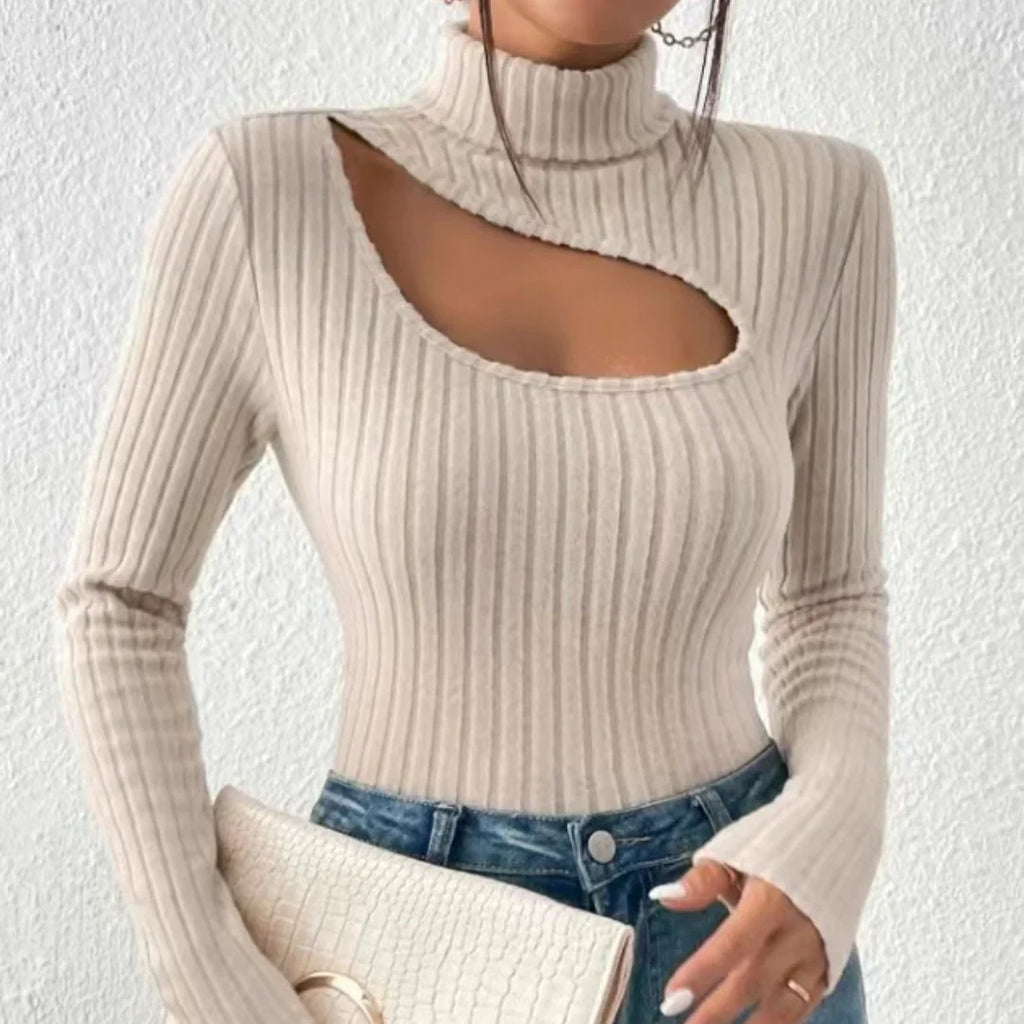 Femme portant un pull beige à col roulé avec découpe asymétrique, tenant une pochette texturée, mode tendance automne, style chic et moderne.