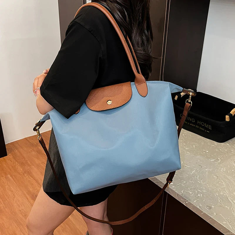 Sac à main bleu avec rabat marron, porté par une femme en robe noire. Accessoire mode élégant, idéal pour le quotidien et les sorties.