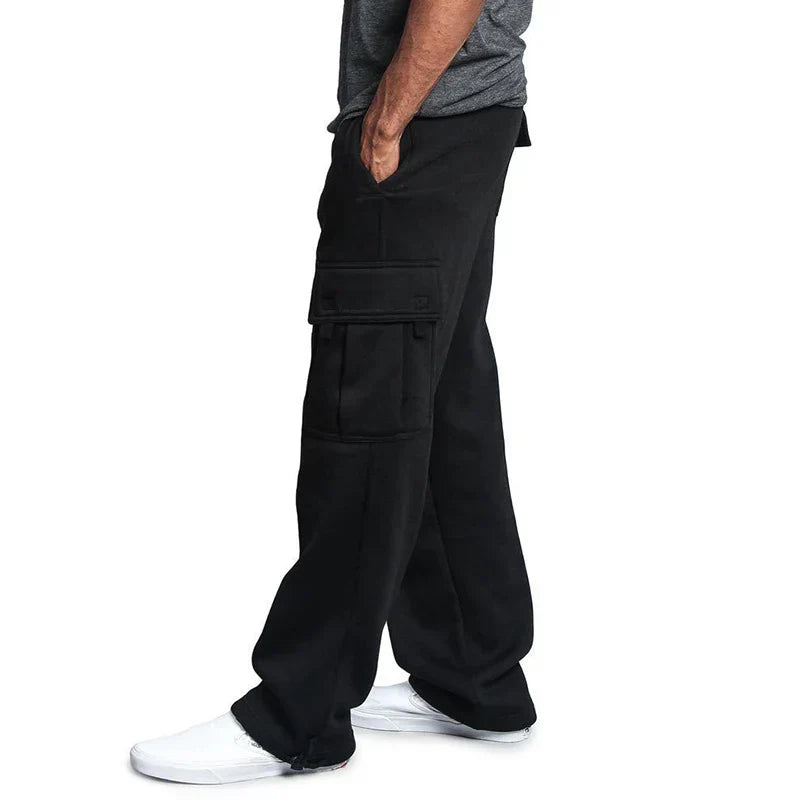 Pantalon cargo noir pour homme avec poches latérales, porté avec un t-shirt gris et des baskets blanches. Mode décontractée masculine.
