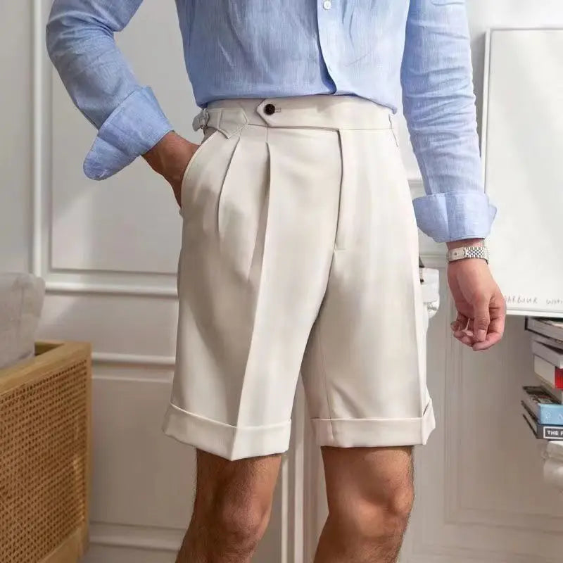 Homme en chemise bleue et short beige élégant, posant dans un intérieur moderne. Mode masculine, tenue estivale chic, style décontracté.
