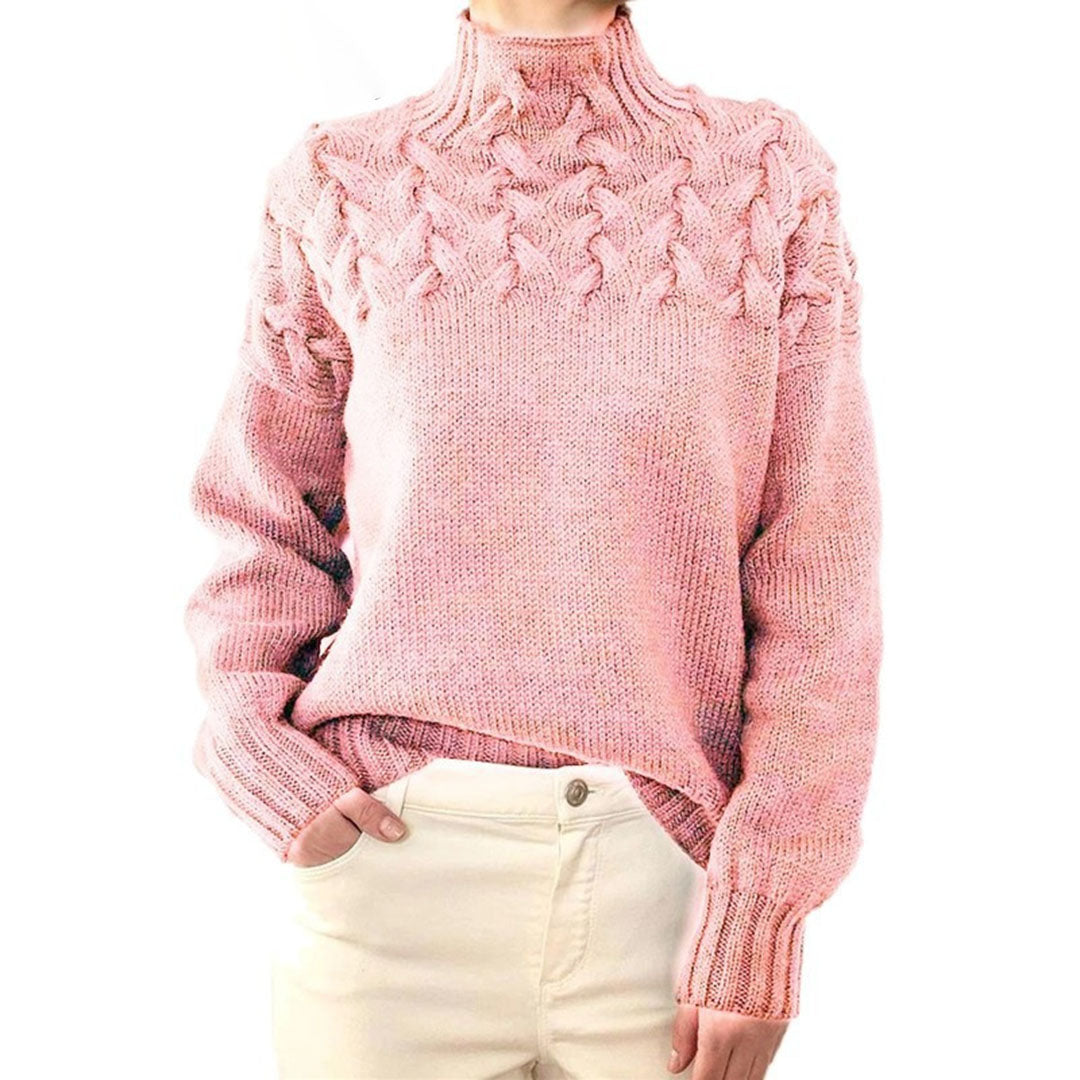 Pull rose en maille torsadée, col montant, manches longues, porté avec un pantalon blanc. Mode femme automne-hiver, style décontracté et élégant.