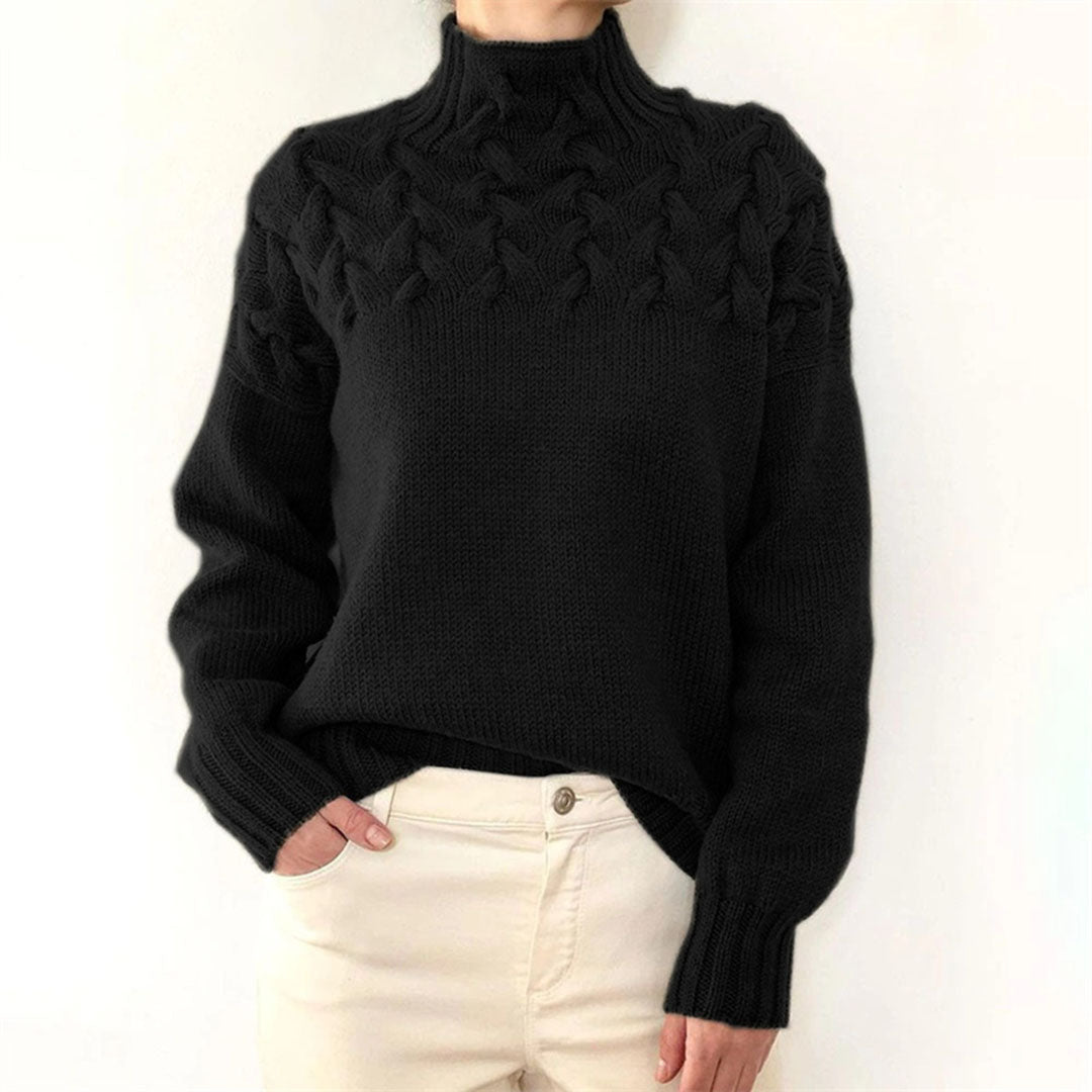 Pull noir en laine torsadée pour femme, manches longues, col montant, porté avec un pantalon beige. Mode hiver élégante et confortable.