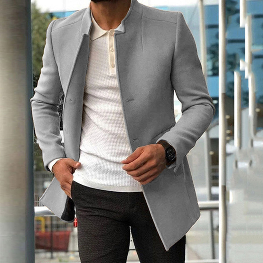 Homme portant un manteau gris élégant, chemise blanche texturée, montre noire; mode masculine moderne, style urbain chic.