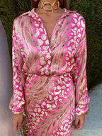 Chemisier et jupe en satin rose à motifs dorés, style léopard, avec col ouvert et manches longues. Accessoire collier doré. Mode élégante et tendance.