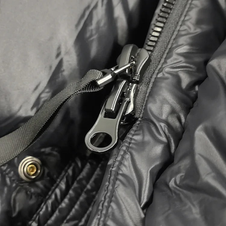 Gros plan d'une fermeture éclair métallique sur une veste noire en nylon, avec un bouton-pression doré visible. Mode, vêtements d'extérieur, accessoires.