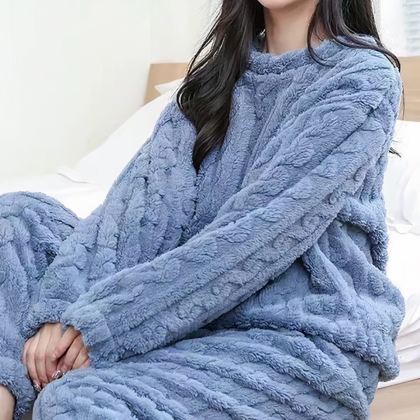 Femme portant un pyjama en polaire bleu, assise sur un lit blanc. Vêtements d'intérieur confortables, mode détente, tenue cocooning.