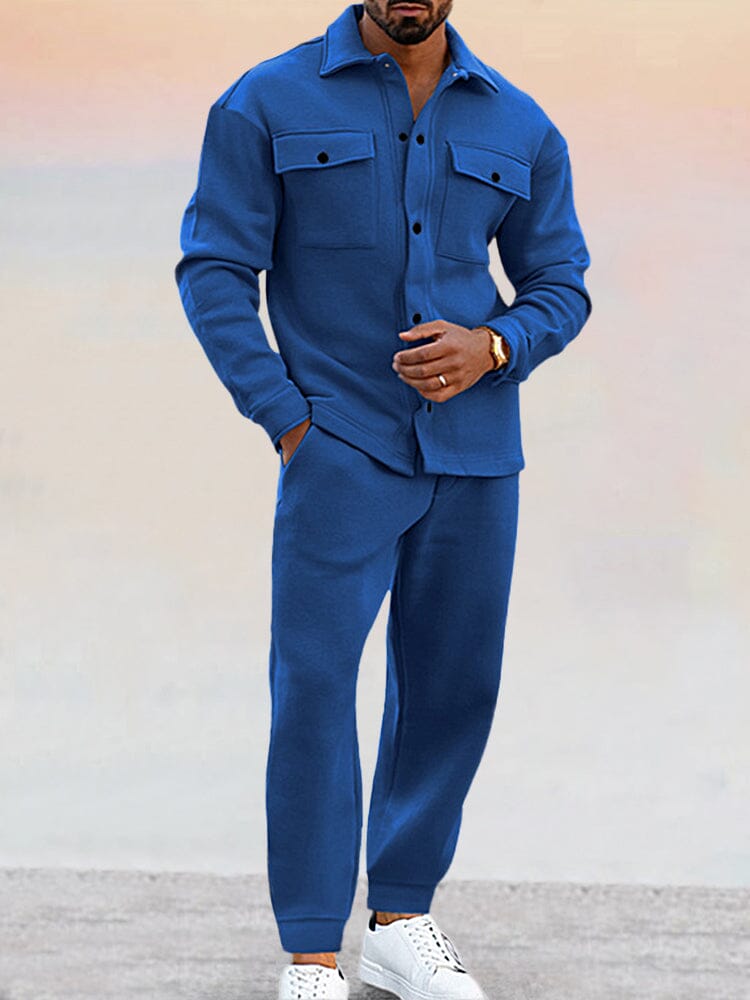 Homme portant un ensemble bleu élégant, chemise à poches et pantalon assorti, chaussures blanches. Mode masculine moderne, tenue décontractée chic.