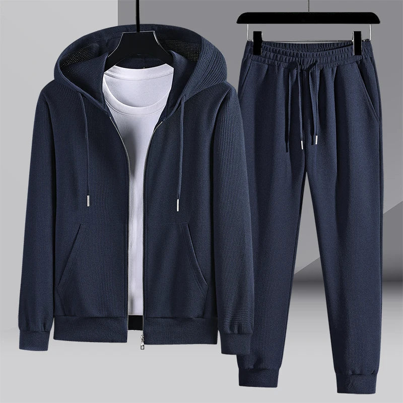 Survêtement bleu foncé pour homme avec capuche, fermeture éclair et poches, accompagné d'un pantalon assorti. Ensemble décontracté et moderne.