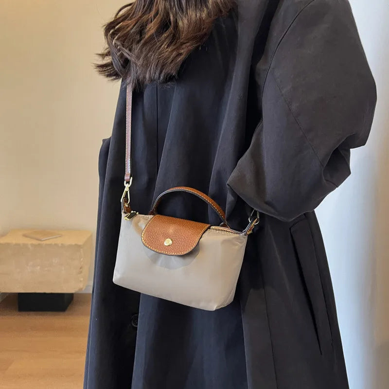 Femme portant un manteau noir avec un sac à main en cuir marron et beige, mode élégante, accessoires tendance, style automne-hiver.