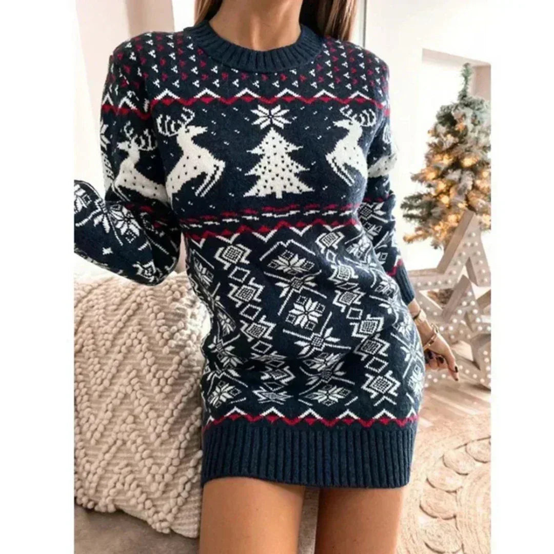 Robe pull de Noël bleue avec motifs de rennes et sapins, femme posant devant un sapin décoré, ambiance festive et hivernale.