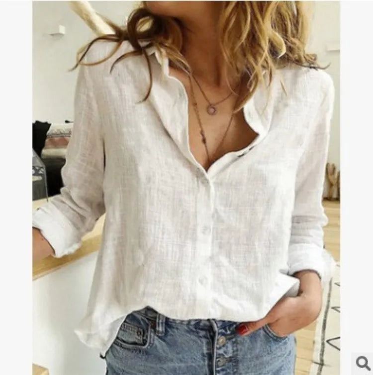 Femme portant une chemise blanche en lin, manches retroussées, avec un collier délicat, posant dans un intérieur moderne. Mode décontractée chic.