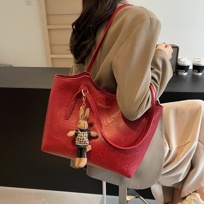 Sac à main rouge élégant avec porte-clés peluche, porté par une femme en manteau beige. Accessoire mode tendance, idéal pour un look chic et moderne.