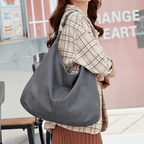 Femme portant un grand sac à main en cuir noir, style décontracté, devant un café urbain. Mode féminine, accessoire tendance, look automnal.
