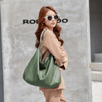 Femme élégante portant un grand sac à main vert en cuir, lunettes de soleil blanches, tenue beige, mode urbaine chic, mur gris en arrière-plan.