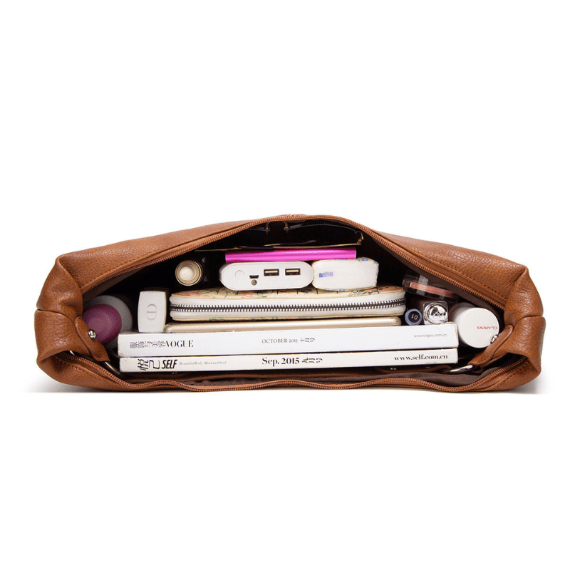 Sac à main en cuir marron ouvert, contenant magazines, chargeur portable, rouge à lèvres, et accessoires divers. Organisation élégante et pratique.