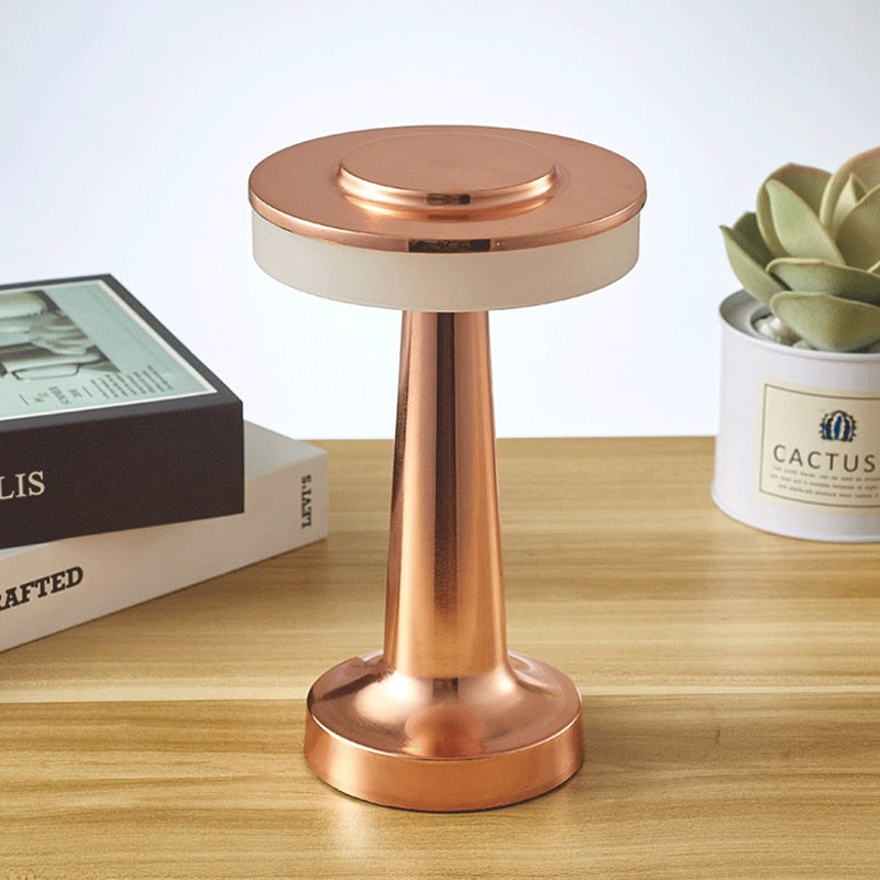 Lampe de table en cuivre moderne sur bureau en bois, à côté de livres et d'une plante en pot. Design élégant, éclairage d'intérieur, décoration contemporaine.