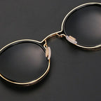 Lunettes de soleil rondes élégantes avec monture dorée et verres noirs, posées sur fond noir. Accessoire mode tendance et chic.