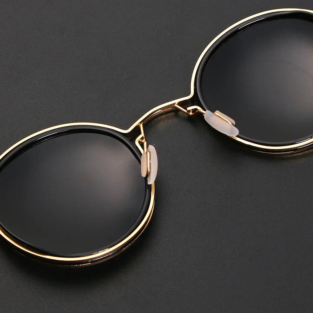 Lunettes de soleil rondes élégantes avec monture dorée et verres noirs, posées sur fond noir. Accessoire mode tendance et chic.