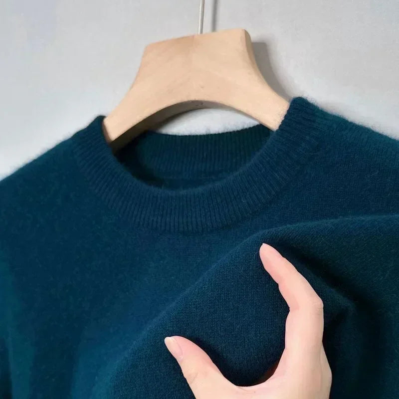 Pull bleu en laine sur cintre en bois, main touchant le tissu doux. Mode hiver, vêtement chaud, col rond, texture confortable.