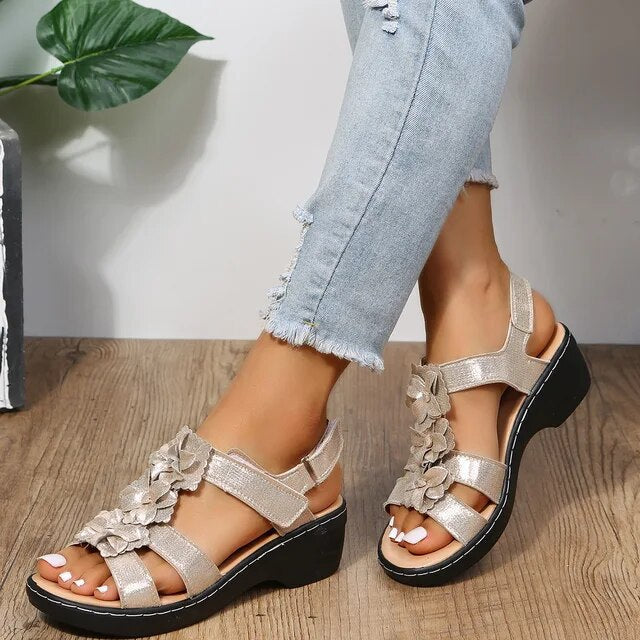 Sandales compensées dorées avec fleurs, portées avec un jean déchiré. Chaussures d'été élégantes pour femmes, confortables et tendance.