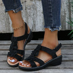 Sandales noires à talons compensés avec fleurs, portées avec un jean déchiré et bracelet doré. Mode féminine, chaussures d'été élégantes.