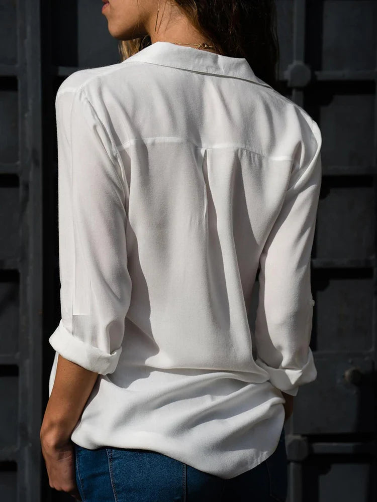 Femme portant une chemise blanche élégante, manches retroussées, devant une porte en métal sombre. Mode féminine, style décontracté chic.