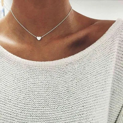 Collier pendentif cœur en argent sur un cou féminin, porté avec un pull blanc texturé. Bijoux élégants, mode féminine, accessoires tendance.