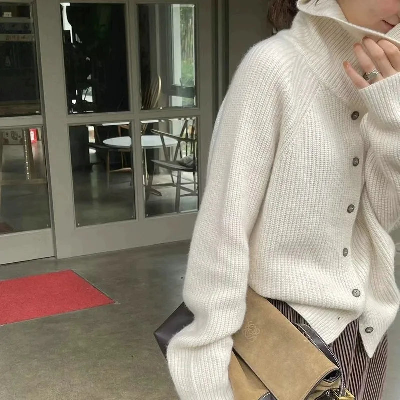 Femme portant un pull en laine blanc à col roulé, tenant un sac en cuir beige. Mode automne-hiver, style décontracté et élégant.