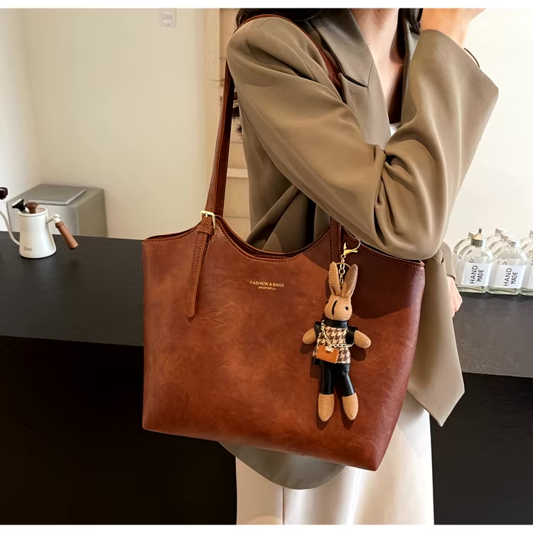 Sac à main en cuir marron avec porte-clés lapin, porté par une femme en blazer beige. Accessoire mode élégant et tendance pour femme.