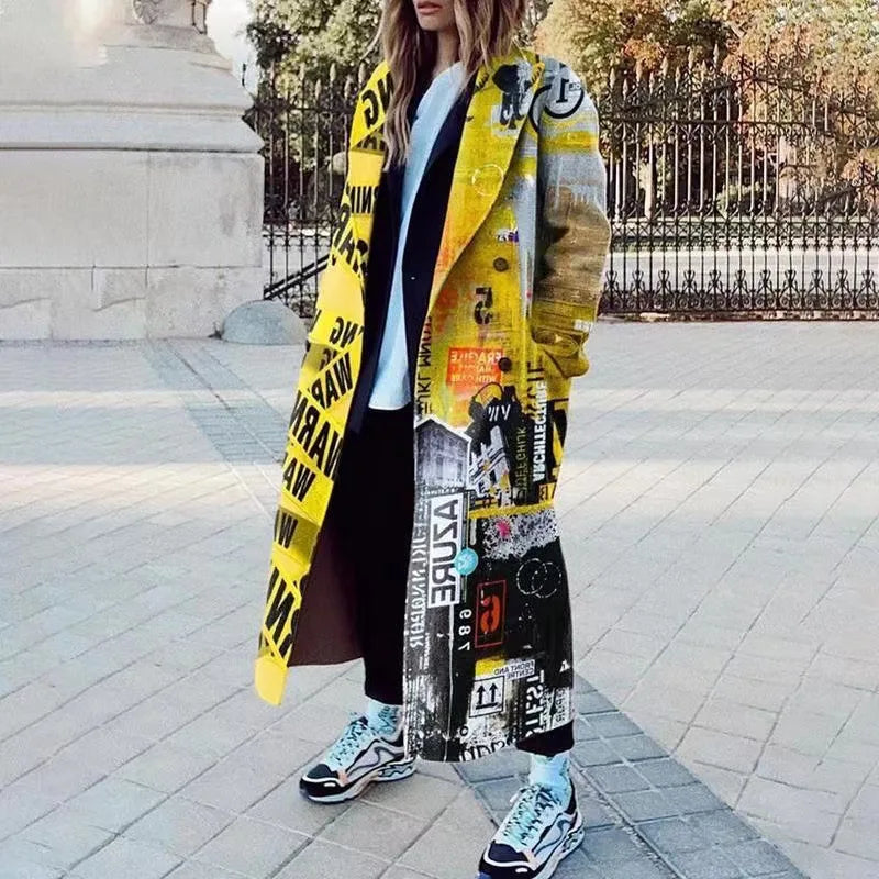 Femme portant un manteau long jaune à motifs graphiques, debout dans la rue. Mode urbaine, style streetwear, tendance automne-hiver.