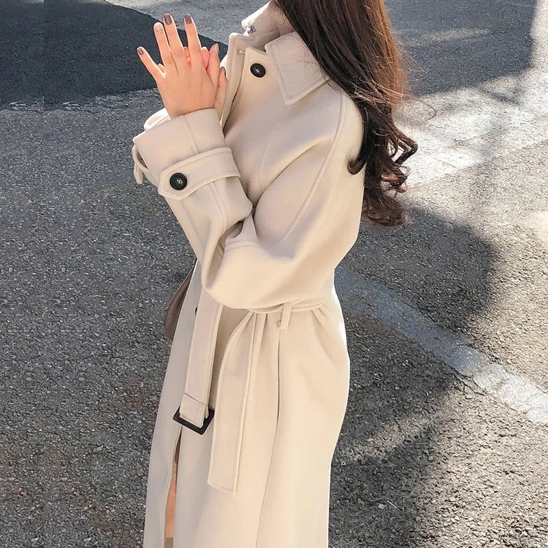 Femme portant un manteau beige élégant, debout sur une route ensoleillée. Mode automne, style chic, vêtements d'extérieur tendance.