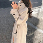 Femme portant un manteau beige élégant, debout sur une route ensoleillée. Mode automne, style chic, vêtements d'extérieur tendance.