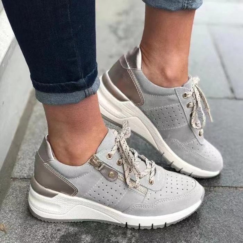 Chaussures de sport grises pour femme avec semelle épaisse, lacets blancs et détails métalliques, portées avec un jean. Mode urbaine tendance.