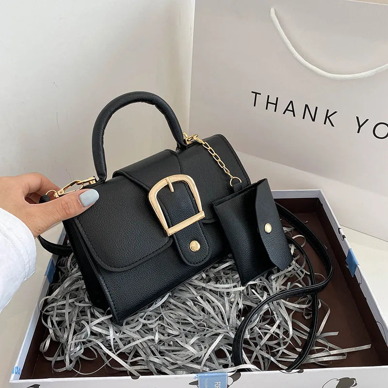 Sac à main noir élégant avec boucle dorée, accompagné d'une pochette assortie. Présenté dans une boîte cadeau avec un sac "Thank You". Accessoire mode chic.