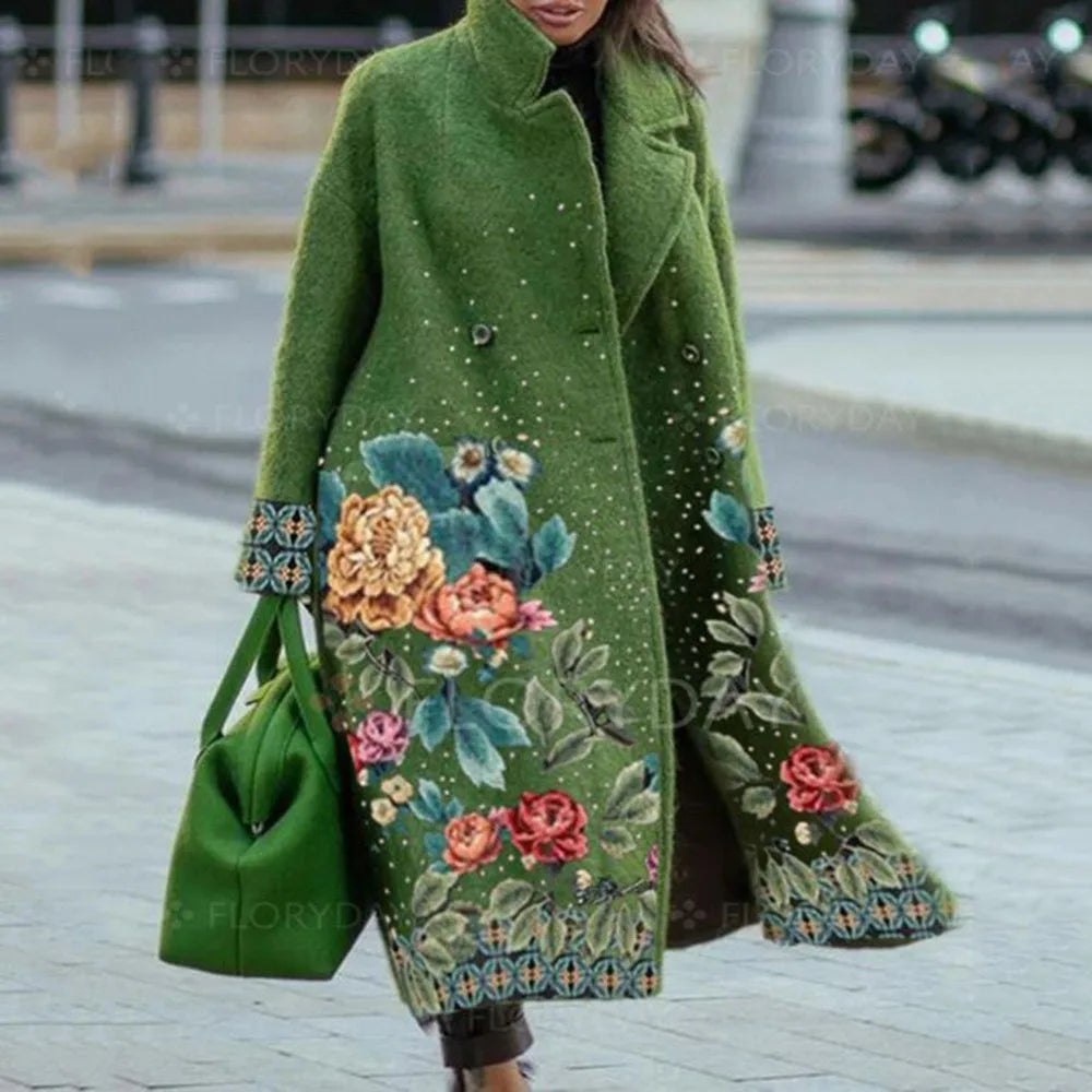 Manteau vert long avec motifs floraux colorés, porté par une femme en extérieur. Sac assorti. Mode automne-hiver, style élégant et tendance.