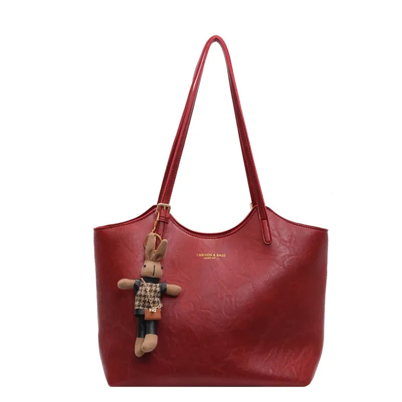Sac à main rouge élégant avec porte-clés peluche lapin, cuir texturé, anses longues, mode femme, accessoire tendance, style chic et moderne.