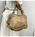 Sac à main en cuir beige porté par une femme en chemise blanche et pantalon à rayures. Mode élégante, accessoire tendance, style chic.